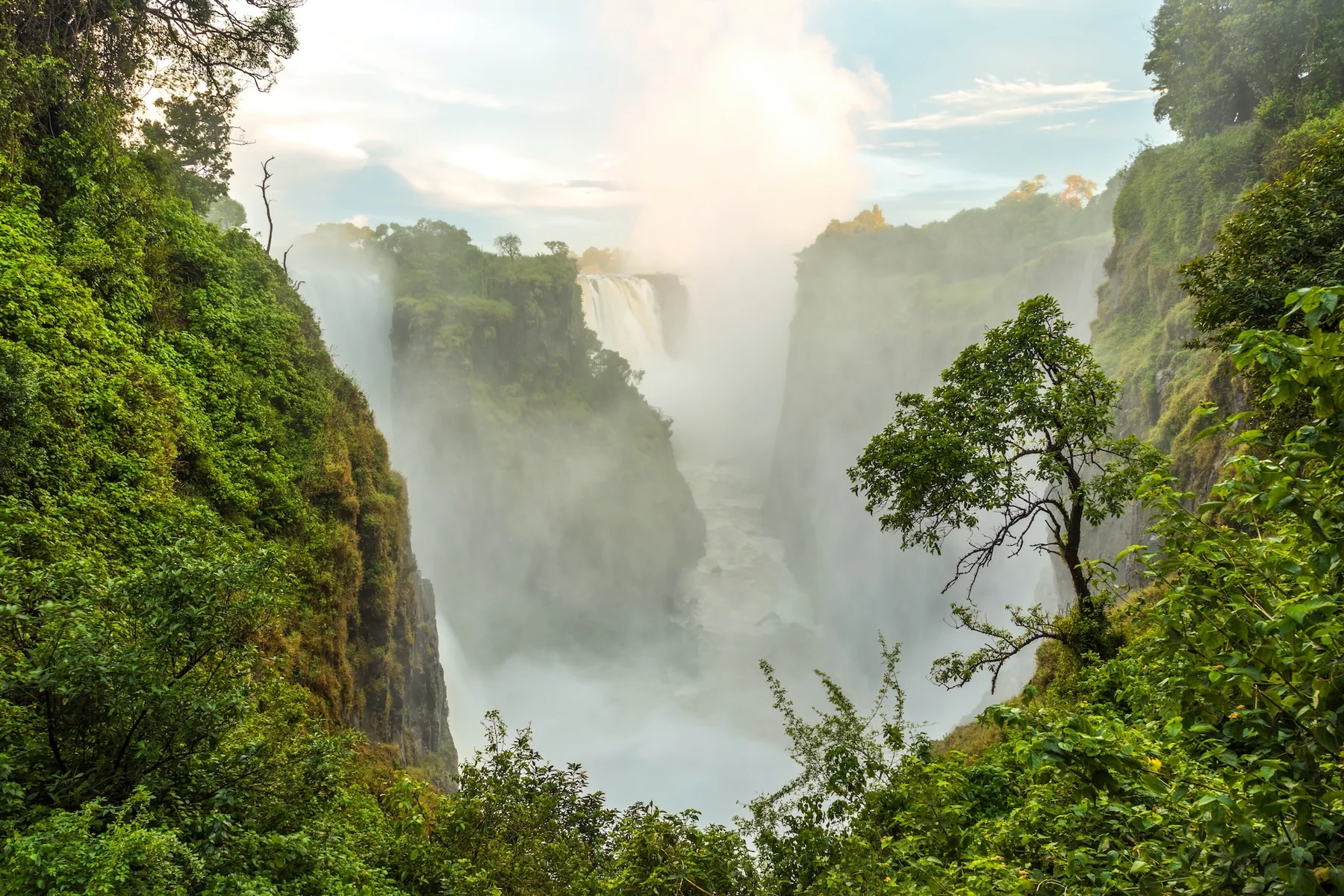 The mist of Victoria Falls surrounded by green cliffs